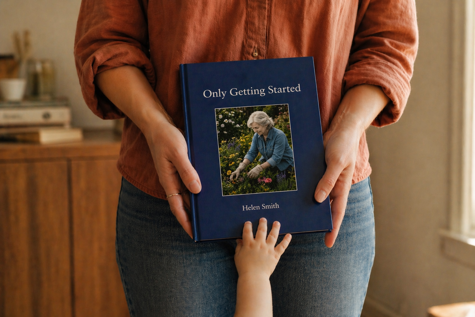 A finished navy Fablr hardcover memoir held in two hands as a small grandchild reaches up to touch it